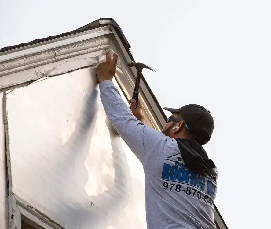 Roofer repairs exterior molding with a hammer on building corner.