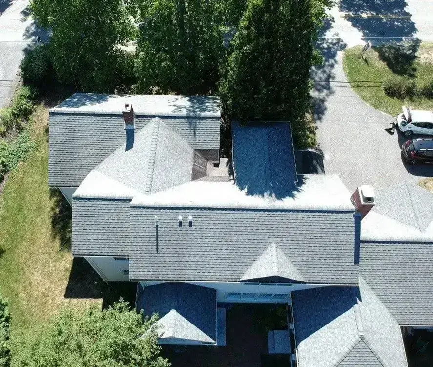 Aerial view of residential roofing surrounded by trees and a driveway.