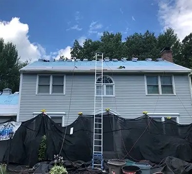 Roofing project underway on a two-story house with protective coverings.