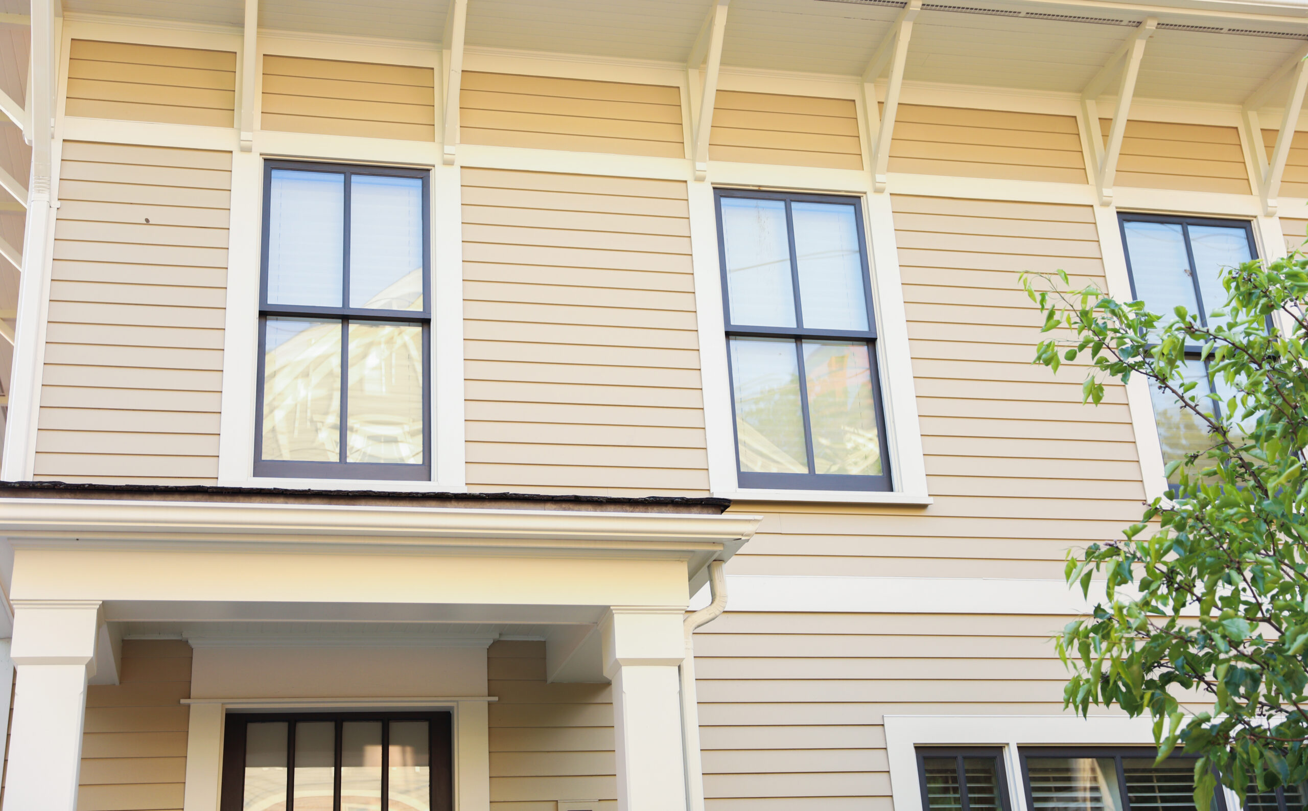 A close-up view of a tan house with gray windows in white frames.