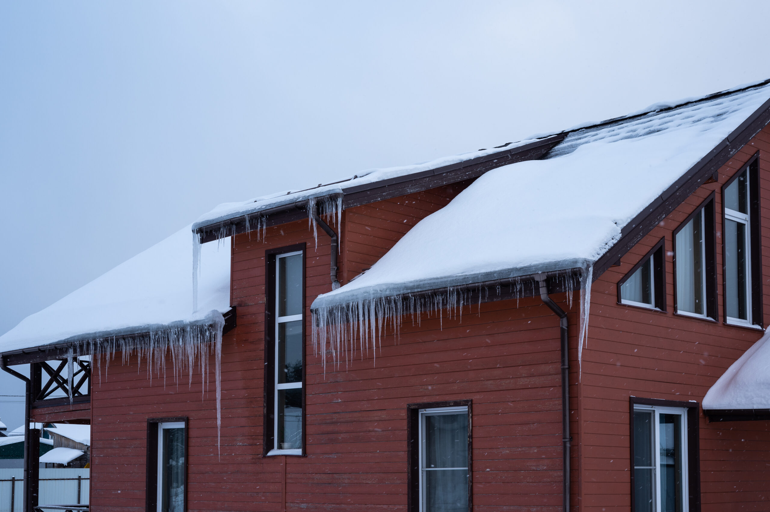 A two-story red house with white windows and snow on the roof.