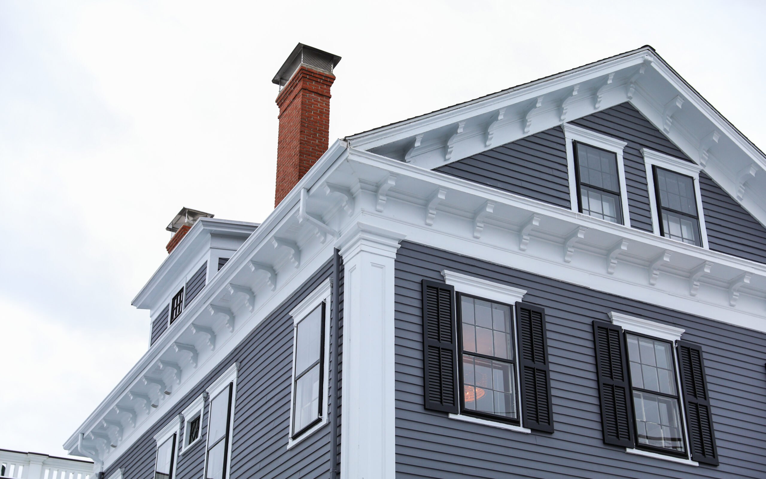 A multi-story gray house with white trim and black windows with black shutters.