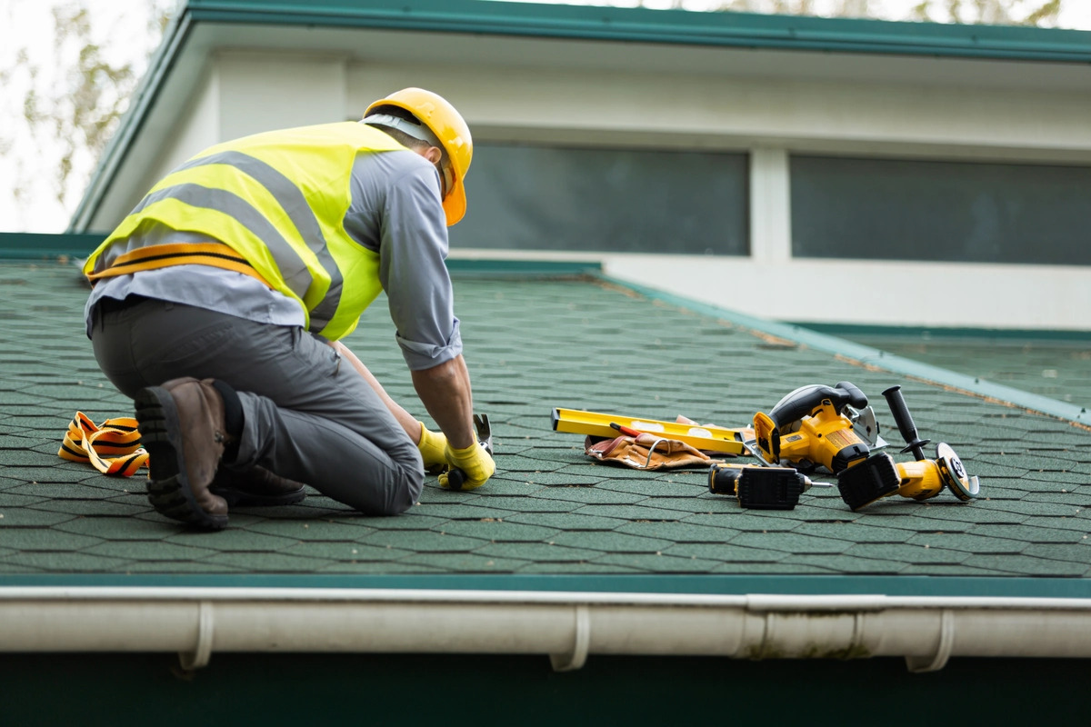A close-up view of black gutters and a black downspout on a white house with an asphalt shingle roof.