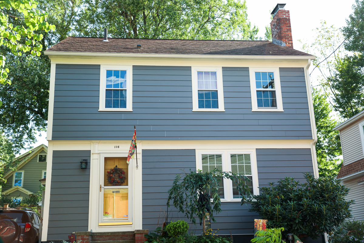 A two-story gray house with a white garage door, white windows, a stone base, and an asphalt shingle roof.