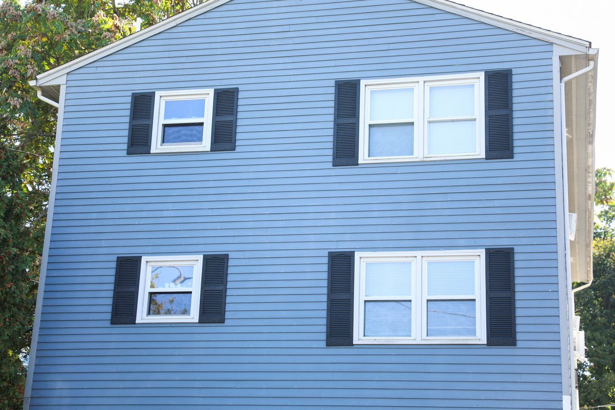 The side of a two-story blue house with white windows and black shutters.