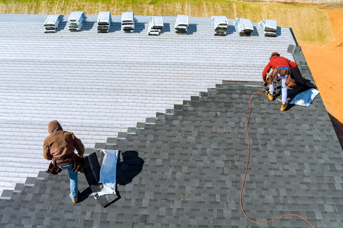 Two roofers nailing new shingles on a roof during a replacement.