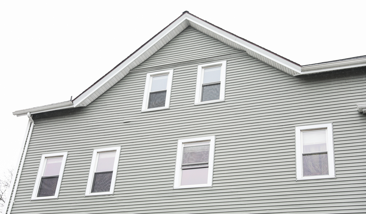 The side of a two-story gray house with white windows.