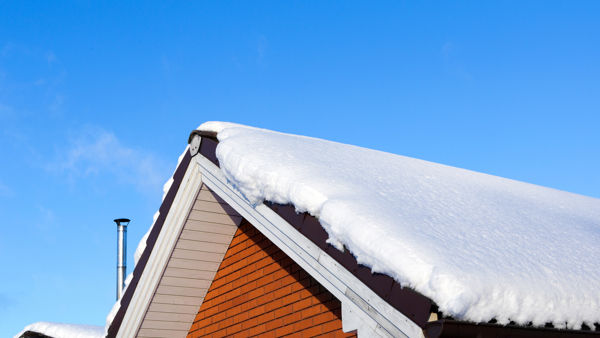 A close-up view of snow on the roof of a brick house.