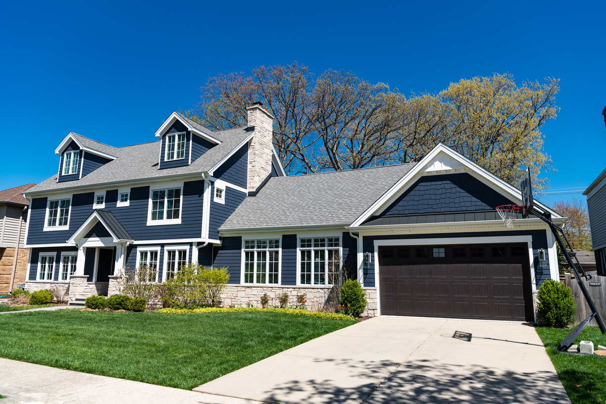 A multi-story blue house with a white base, a brown garage door, white windows, and an asphalt shingle roof.