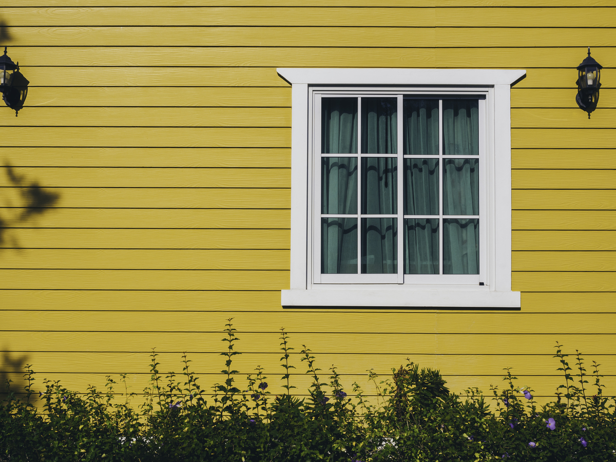 The side of a yellow house with a white window.