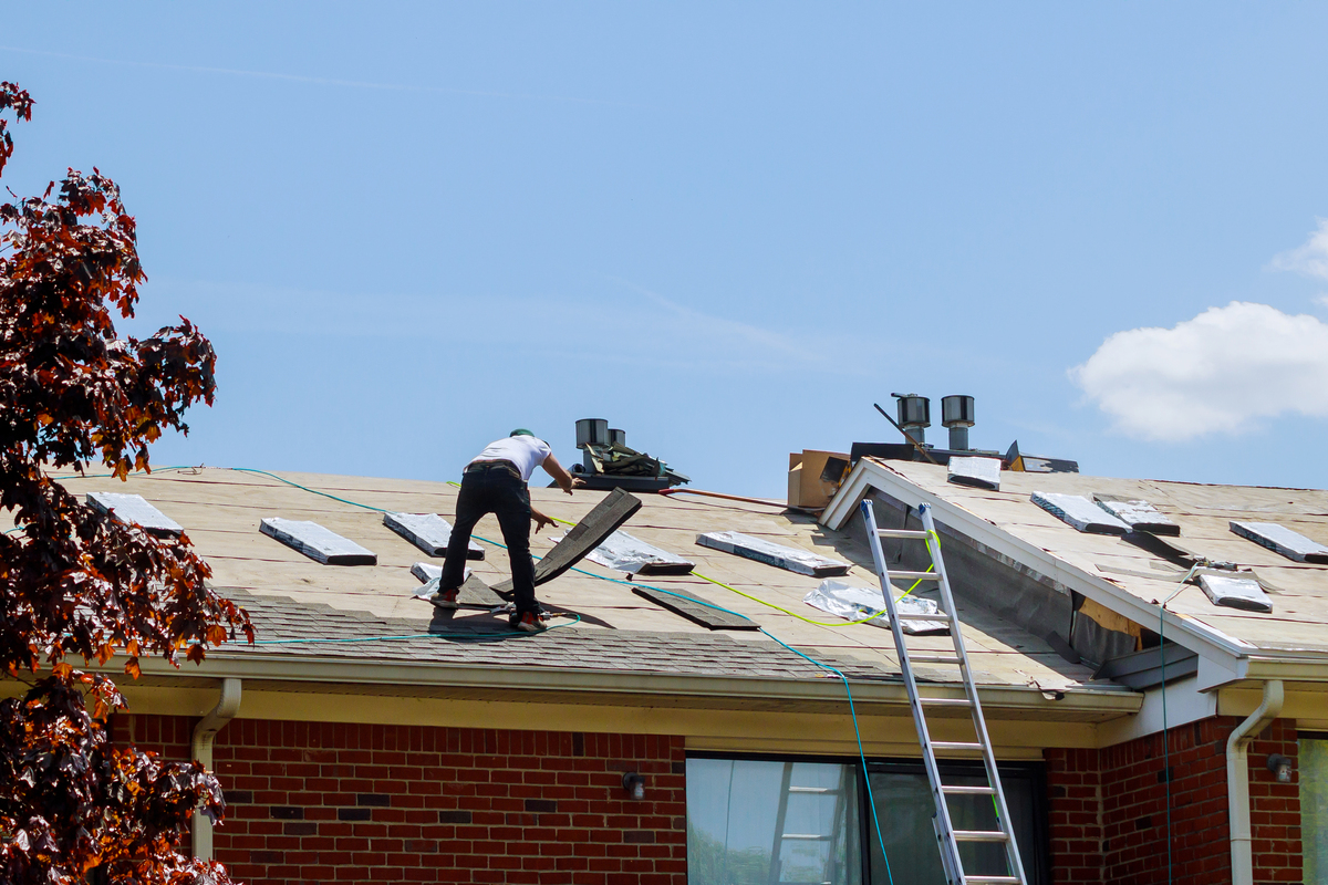 A roofer in the process of a roof replacement on a brick house.