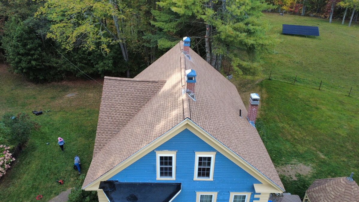 An aerial view of a blue house with white windows and an asphalt shingle roof.