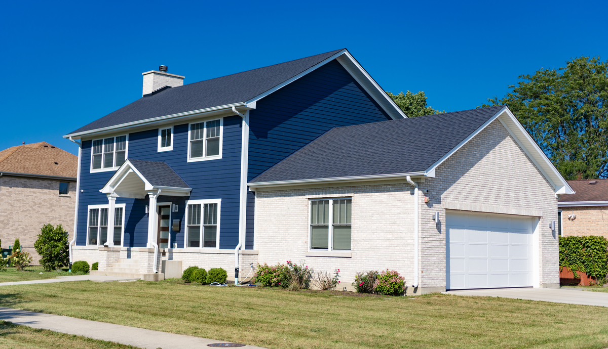 A close-up view of black gutters and a black downspout on a tan house with an asphalt shingle roof.