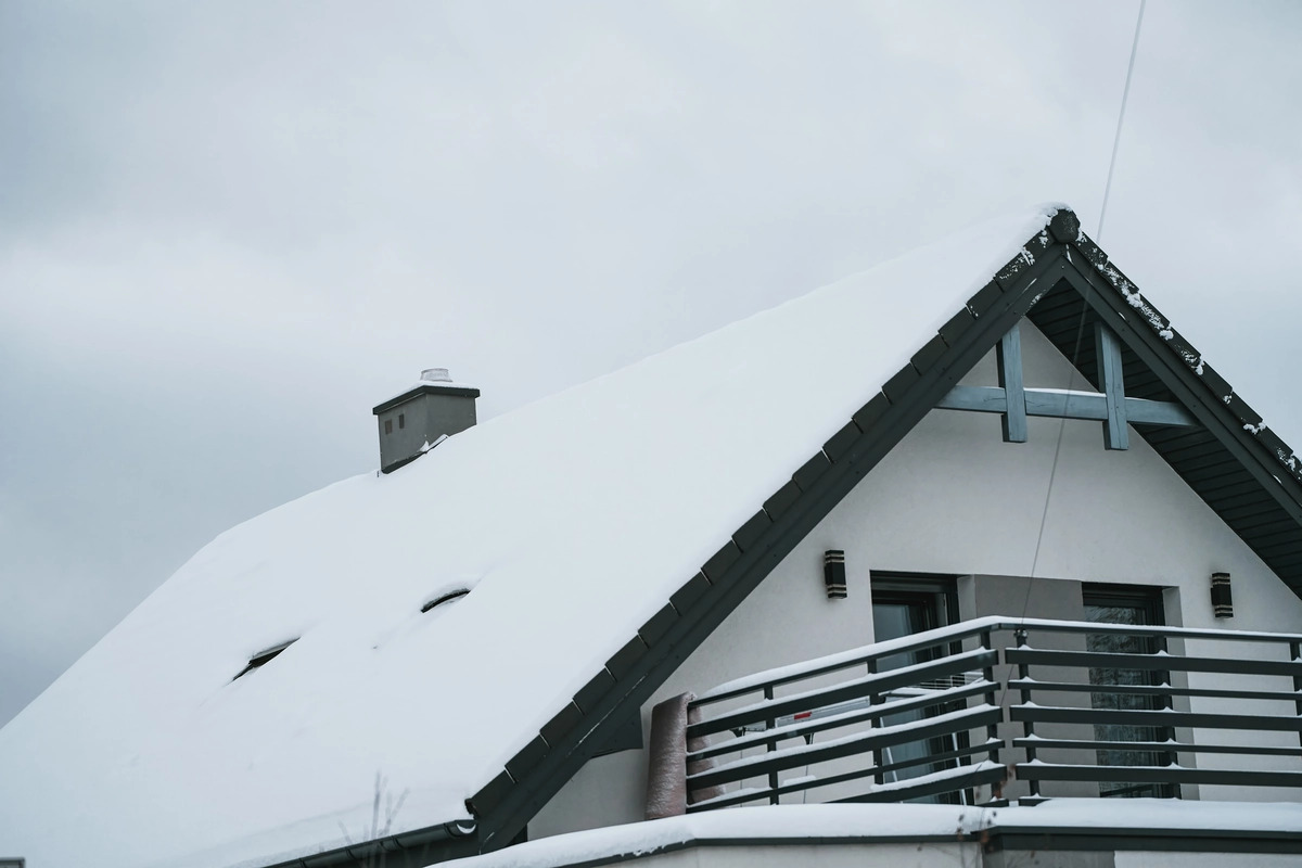 A close-up view of a gray house with white windows and an asphalt shingle roof.