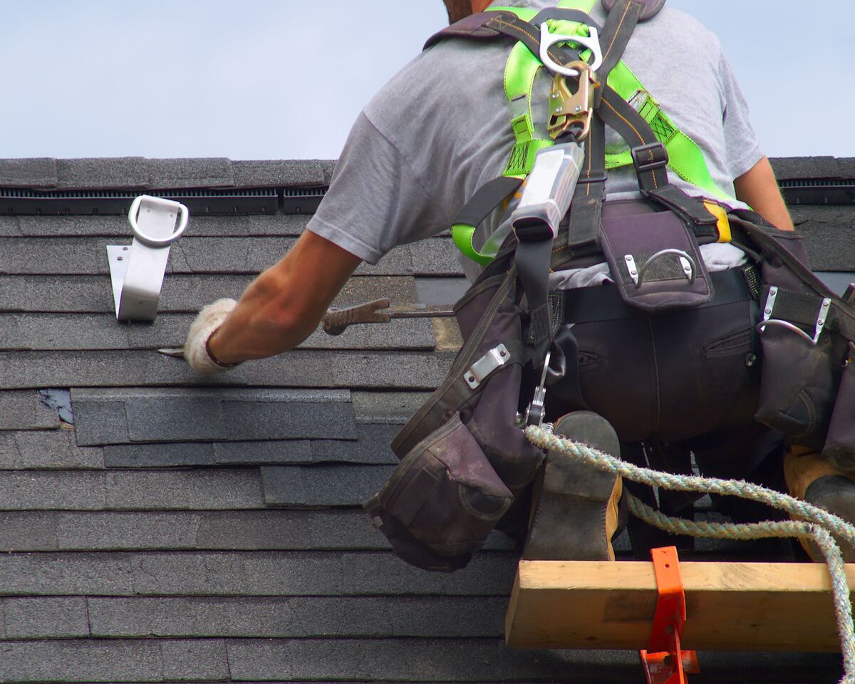 A close-up view of a roofer in safety equipment making repairs to a roof near the peak.