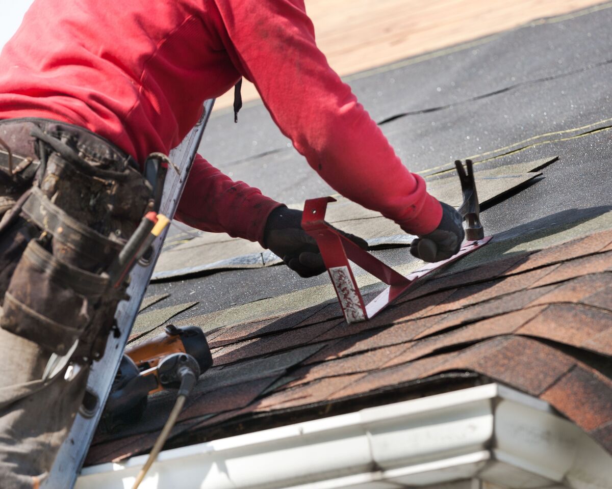 A close-up view of a roofer nailing new shingles on a roof during a replacement.