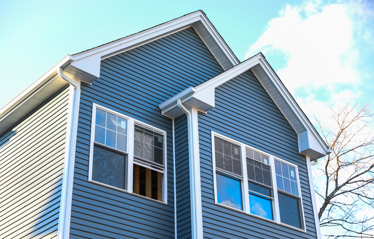 The side of a two-story blue house with white windows and white gutters.