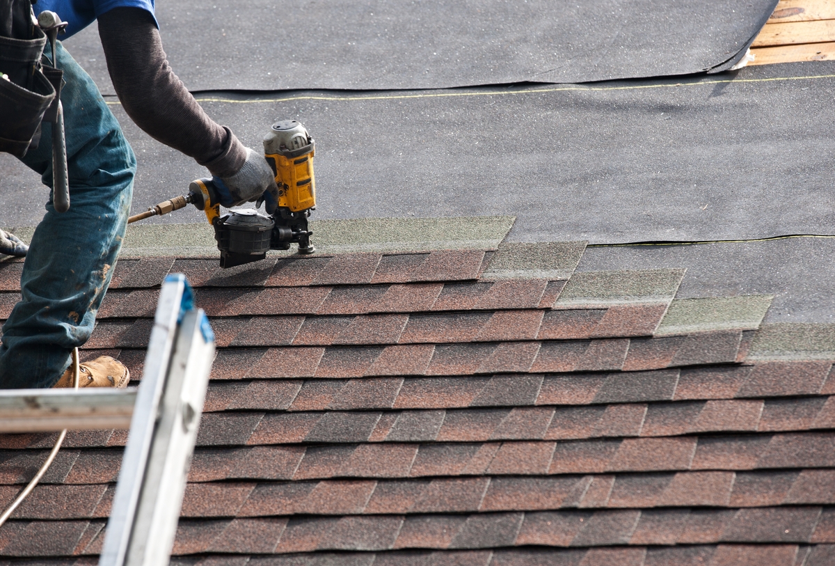 An upward view of a roofer on a ladder making repairs.