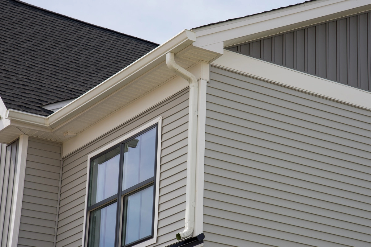 A close-up view of the upper floor of a gray house with white windows.