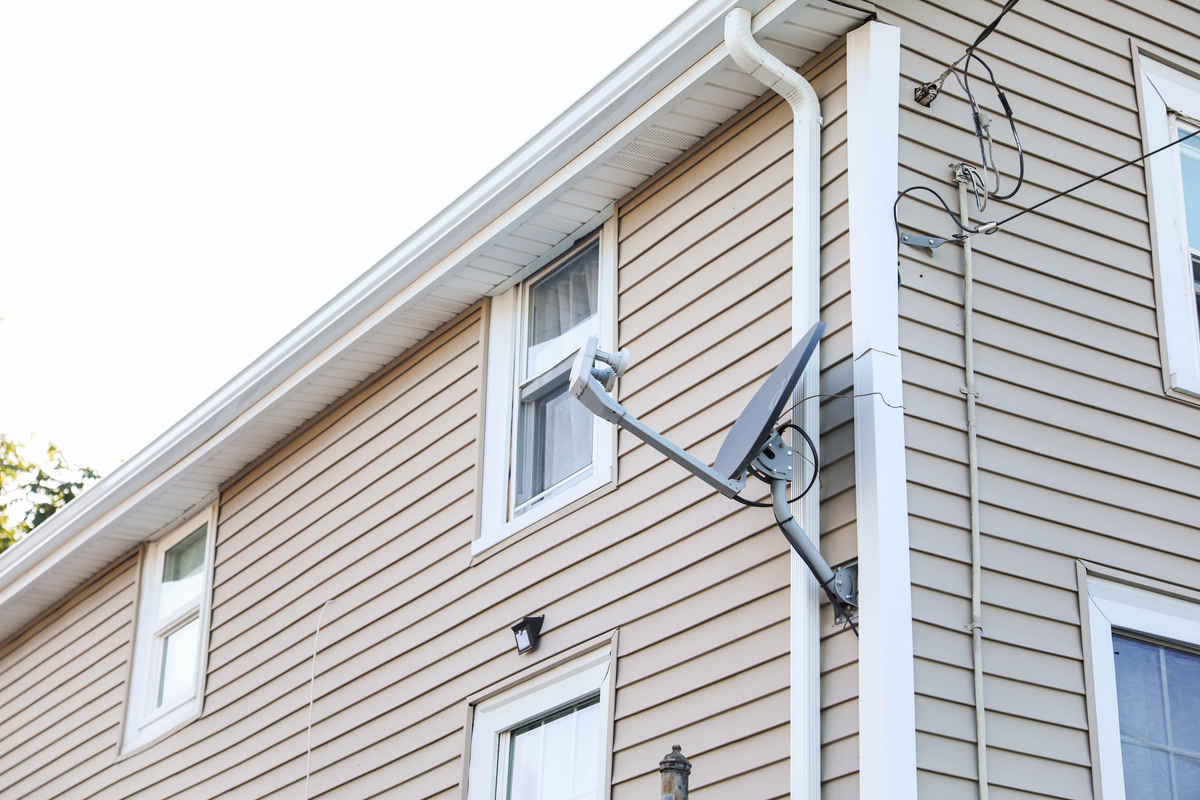 The back of a tan house with white windows, white gutters, and a satellite dish.