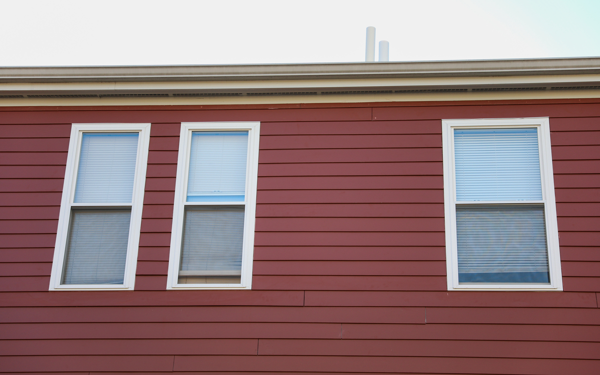 A close-up view of a red house with three white windows.